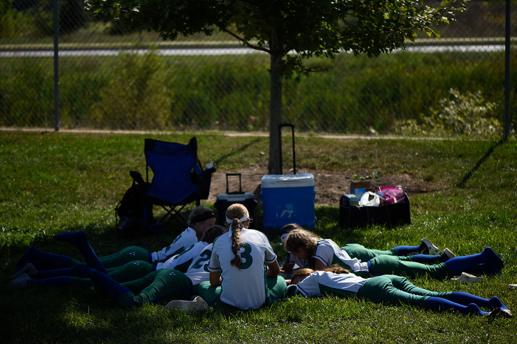 Members of the Blue Springs South High School softball team gather around in the shade between games